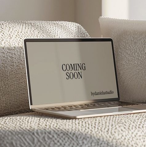 A sleek laptop on a textured cream sofa displaying a “COMING SOON” message in a minimalist neutral-toned room.written on screen